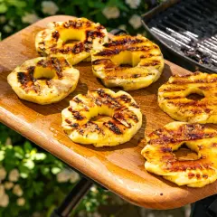 Gegrillte Ananasscheiben mit karamellisierten Rändern auf einem Holzbrett, bereit zum Servieren. Das Ananas grillen bringt süße Aromen hervor.