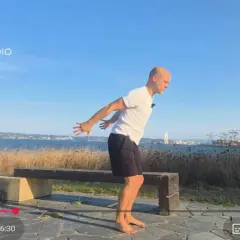 Hombre practicando yoga tibetano al aire libre, con el mar y la ciudad de fondo.