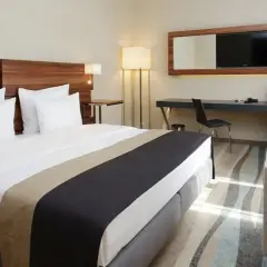 Nowoczesne wyposażenie pokoi hotelowych: wygodne łóżko, biurko z TV, fotele i stolik.