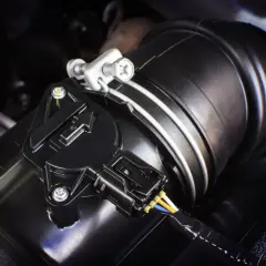 Schwarzer Ladedrucksensor mit Kabeln an einem Ansaugschlauch im Motorraum.