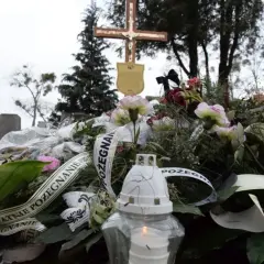 Wieniec pogrzebowy z krzyżem i płonącą świecą na cmentarzu.
