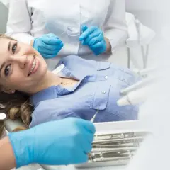 Uśmiechnięta pacjentka w gabinecie stomatologicznym, dentysta wykonuje zabieg.