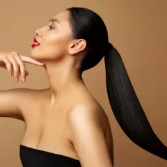 Frau mit glatten, schwarzen Haaren nach hinten gebunden, die ihr Gesicht und ihre Schultern umrahmen. Sie trägt roten Lippenstift.