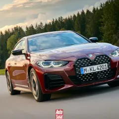 Czerwone BMW G26 z charakterystycznym grillem pędzi po krętej drodze wśród zielonych wzgórz i lasów.