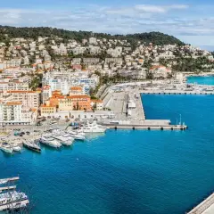 Vue panoramique du port de Nice, avec des yachts amarrés et des bâtiments colorés. On imagine un repas chez Juliette, menu ensoleillé.