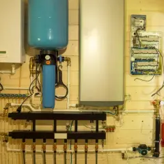 Système de chauffage avec chaudière, ballon tampon sur retour PAC, et tableau électrique sur mur en bois.