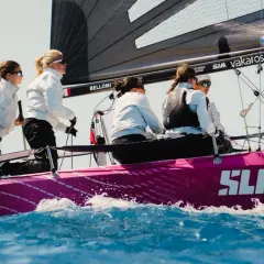 Equipaggio femminile su barca a vela rosa, con la vela nera e il logo SLAM. Le veliste si preparano per la regata RS 21.