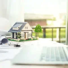 Model domu, plany, kask budowlany i laptop. Planujemy wspólny kredyt na dom na działce męża.