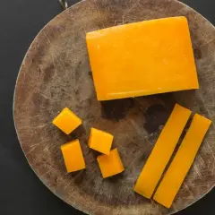 Un bloque de queso color naranja, cortado en cubos y bastones, sobre una tabla de madera.