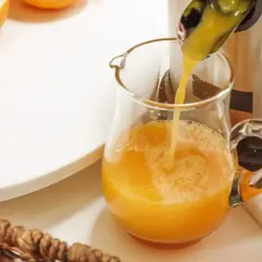 Frisch gepresster Orangensaft fließt in ein Glas. Orangen sind bereit, um zu zeigen, was man entsaften kann.