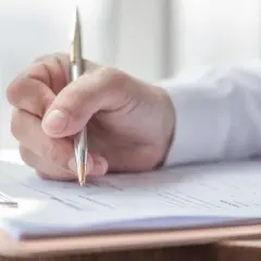 Dłoń pisze długopisem na dokumencie. To może być część inwentaryzacji, która wyjaśnia, co to jest.