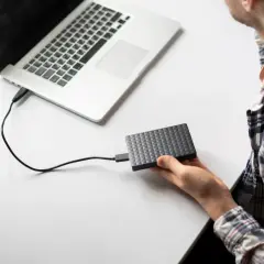 Chłopak podłącza dysk zewnętrzny do laptopa. Prosty sposób, jak podłączyć dysk zewnętrzny do laptopa, by przenieść dane.