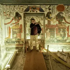 Un hombre posa en la tumba de Nefertari, rodeado de vibrantes jeroglíficos y figuras divinas que narran su viaje al más allá.