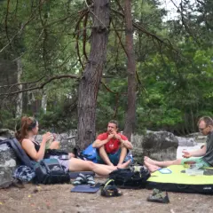 Drei Kletterer machen eine Pause im Wald von Fontainebleau. Ein Mann isst, während die anderen sich ausruhen.