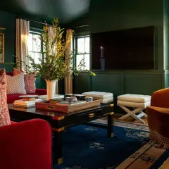 A rich, jewel-toned living room with plush red sofas, an orange velvet armchair, and a dark coffee table, showcasing timeless interior design.