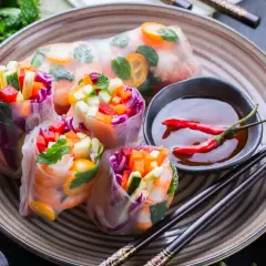 Kolorowe spring rolls z krewetkami, warzywami i miętą, podane z sosem chili i limonką. Pyszna przekąska.
