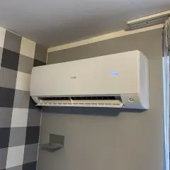 Biały klimatyzator Haier zamontowany na ścianie z szarą tapetą w kratę.