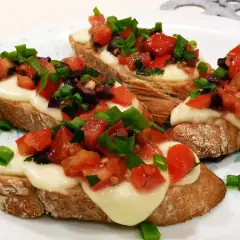 Bruschetta z pomidorami i mozzarellą: chrupiące grzanki z roztopionym serem, świeżymi pomidorami, oliwkami i szczypiorkiem. Idealny przepis na szybką przekąskę.