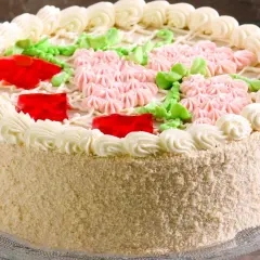 Tort ozdobiony kremem, różowymi kwiatkami, zielonymi listkami i czerwonymi galaretkami. Pyszny krem do tortu zachwyca smakiem.