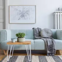 A light blue couch with a throw blanket and pillow. A small wooden table with a plant sits on the couch. This image shows how to clean a couch.