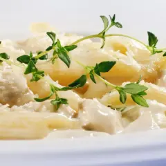 Penne z kurczakiem w kremowym sosie jogurtowym, posypane parmezanem i udekorowane gałązkami tymianku.