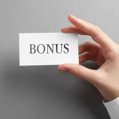 Dłoń trzyma kartkę z napisem "BONUS". To może być dodatek stażowy, który czeka na Ciebie!