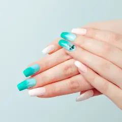Dłonie z paznokciami ombre w odcieniach turkusu i bieli. Jedna z płytek zdobiona jest cyrkoniami. Zastanawiasz się, top coat co to? To warstwa nabłyszczająca i utwardzająca manicure.