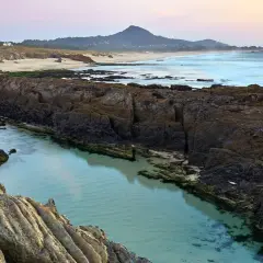 Aguas cristalinas en la **playa das Furnas**, entre rocas volcánicas y arena dorada, con el mar al fondo y una montaña.