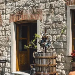 Ingresso di "Cinque Quinti", un negozio di degustazione con un torchio antico e vasi di fiori rossi.