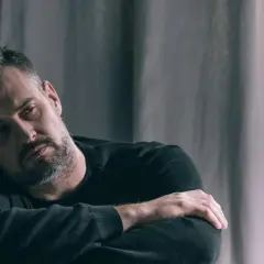 Mężczyzna oparty o ścianę, zamyślony, z rękami skrzyżowanymi na piersi. Może to być obraz osoby zmagającej się z problemami, szukającej ukojenia, jak po zażyciu paroxinor.