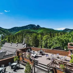 Klimatyczny hotel w górach z tarasem widokowym. Widać drewniane meble, góry i las.
