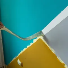 Hand entfernt Klebeband, um eine scharfe Kante beim Farbe streichen zu erzielen. Türkis trifft auf Grau und Ockergelb.