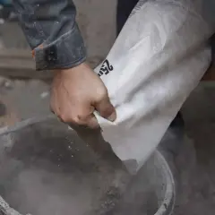 Ręce wsypują cement z worka do wiadra. Różne rodzaje cementu czekają na użycie.