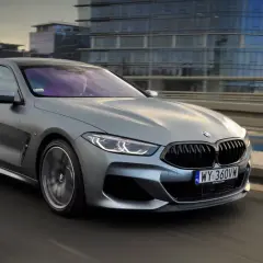 Srebrne BMW M850i sunie po moście, odbijając światła miasta w swoich lśniących szybach.
