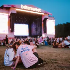 Para na trawie przed sceną festiwalu Bittersweet 2026. W tle tłum i wielkie ekrany.