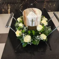 Białe róże i gipsówka otaczają urnę z krzyżem. Kwiaty na pogrzebie z urną symbolizują pamięć i szacunek.