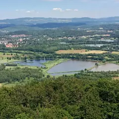 Krajobraz z lotu ptaka: rozległe stawy podgórzyńskie otoczone zielenią, z miasteczkiem w tle i pagórkami w oddali.