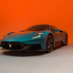 Niebieski Maserati MC20 z charakterystycznym logo na grillu, prezentowany na tle pomarańczowego gradientu.