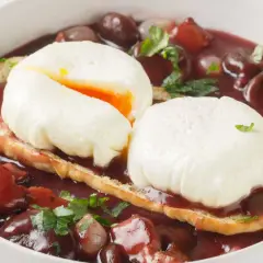 Un œuf meurette, deux œufs pochés sur toast, baignant dans une sauce au vin rouge avec lardons et oignons.