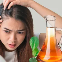 Mujer preocupada revisa su cabello. A su lado, una botella de vinagre de manzana para el pelo y una manzana roja.