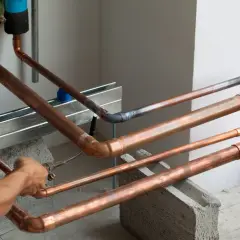 Instalator pracuje nad miedzianymi rurami, tworząc skomplikowaną sieć, niczym w zawiłych układach pole dance duety.