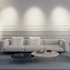 Elegante salón con sofá blanco, mesas de centro y una lámpara de pie sin pantalla que ilumina la pared con molduras.