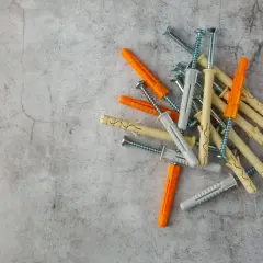 Montón de tacos de pared de plástico y tornillos. Hay varios tipos de tacos de pared, de colores naranja, gris y beige, listos para fijar objetos.