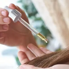 Dłoń trzymająca pipetkę z olejkiem nad pasmem włosów.