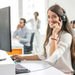 Eine freundliche Callcenter-Mitarbeiterin lächelt in die Kamera. Sie sitzt am Schreibtisch und spricht ins Headset. Sie hilft Kunden, die vielleicht auch mal Werbung widersprechen möchten.