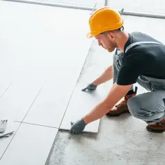Fachowiec w żółtym kasku układa płytki. Zastanawiasz się, ile kosztuje położenie płytek za metr?