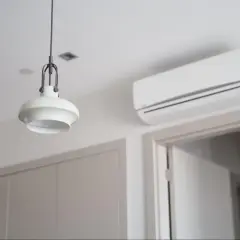 Biały klimatyzator ścienny nad drzwiami, obok wiszącej lampy.