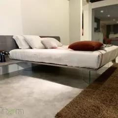 Un letto sospeso come funziona: design moderno con testiera in legno, comodino integrato e gambe in vetro trasparente.