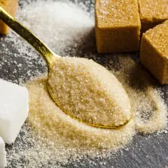 Łyżeczka brązowego cukru na tle kostek białego i brązowego cukru.