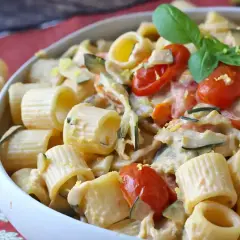 Piatto cremoso di pasta con zucchine, pomodorini e Philadelphia, guarnito con basilico fresco.